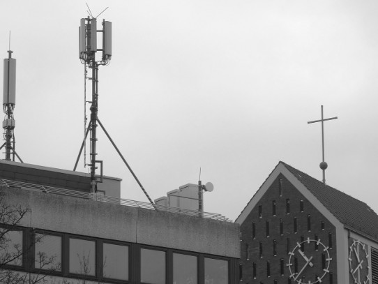 Kreuz auf einer Kirche und Funkzellenanlage auf einem Haus
