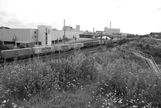 Blick vom höchsten Punkt des Lärmschutzwalls der Brache am Ende der Godehardstraße in Bremen, Hemelingen, auf die Bahnlinie, den Hallenkomplex mit dem Kaufhaus und die Industrieanlagen.