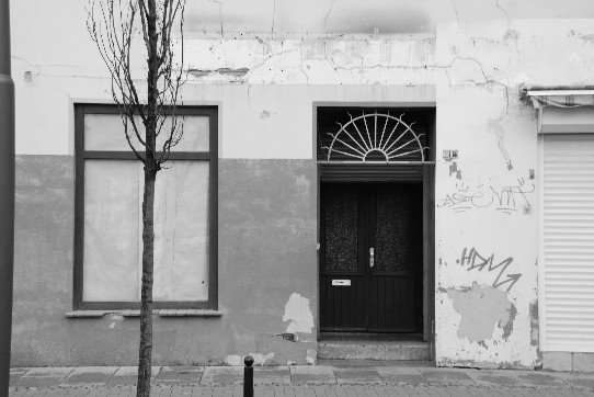 A large window taped shut with paper, a shadow of a dismantled illuminated advertising above an entrance of a shut down shop